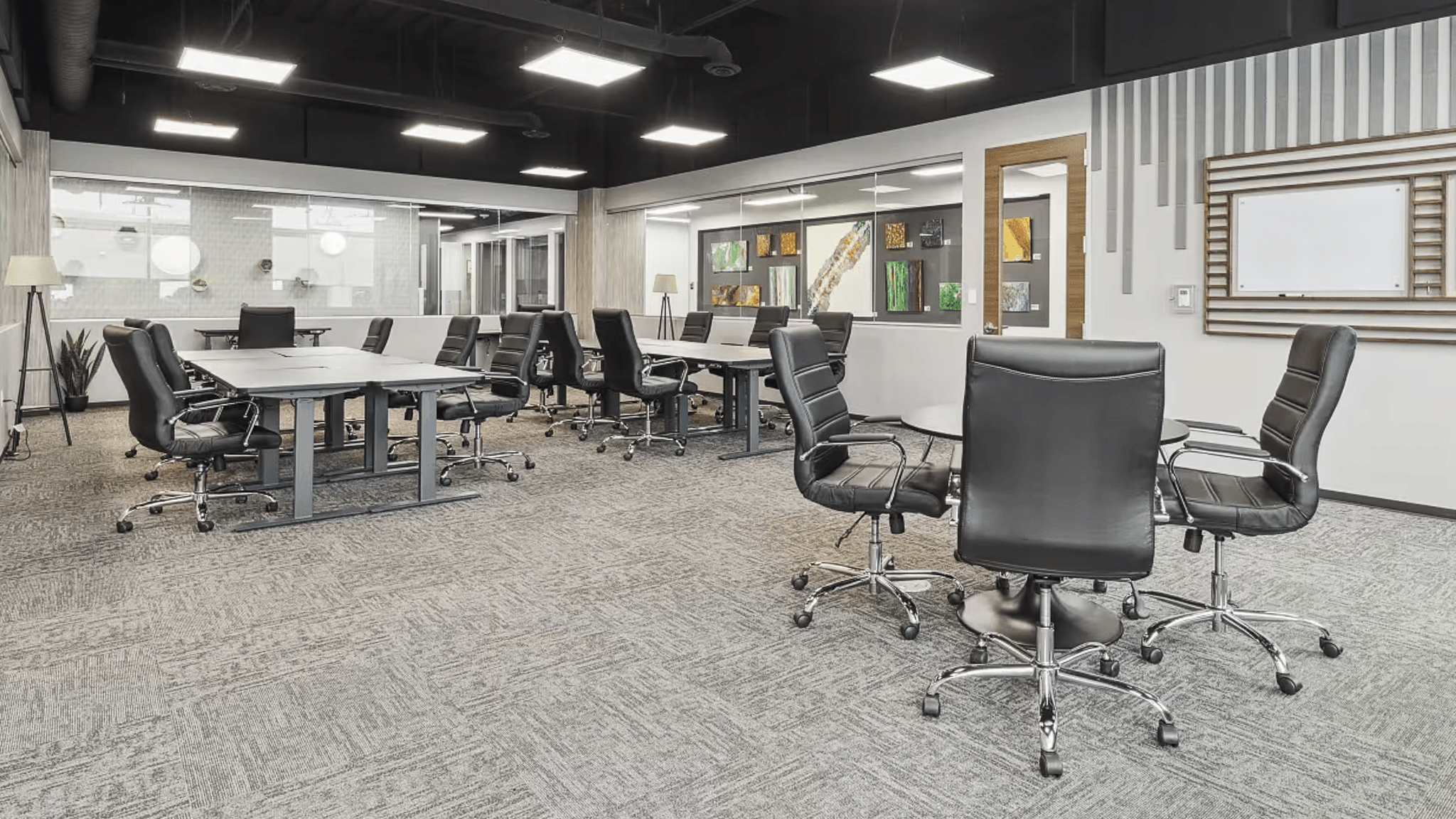 Large team suite with rows of black task chairs, glass partitions, and whiteboard wall