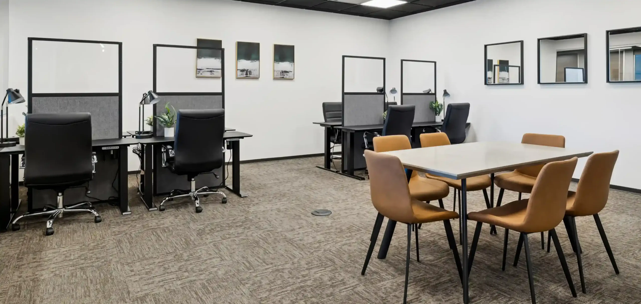 Private office with two desks and task chairs, framed art on white walls, and a small meeting table with tan chairs