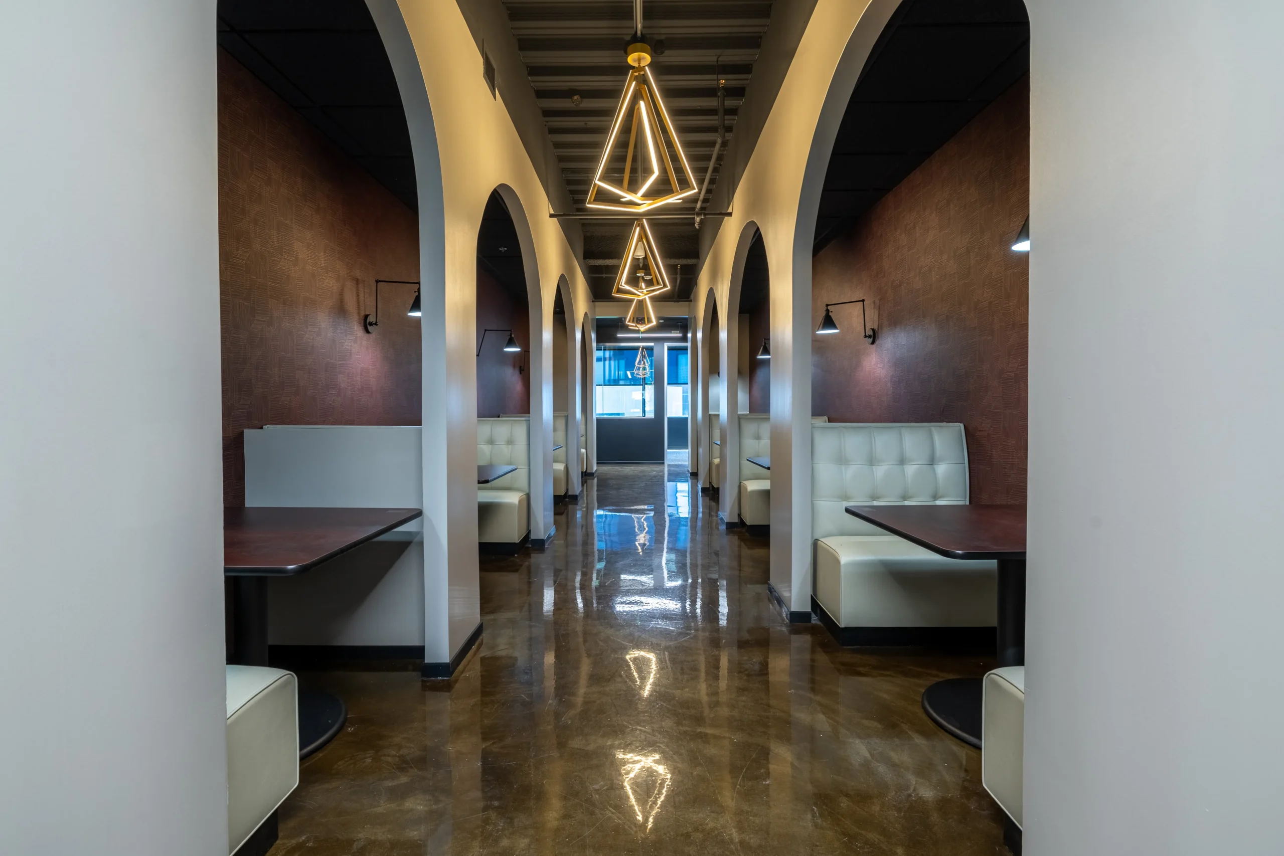 Lounge area with arched alcoves, upholstered bench seating, a geometric pendant light, and a polished tile floor