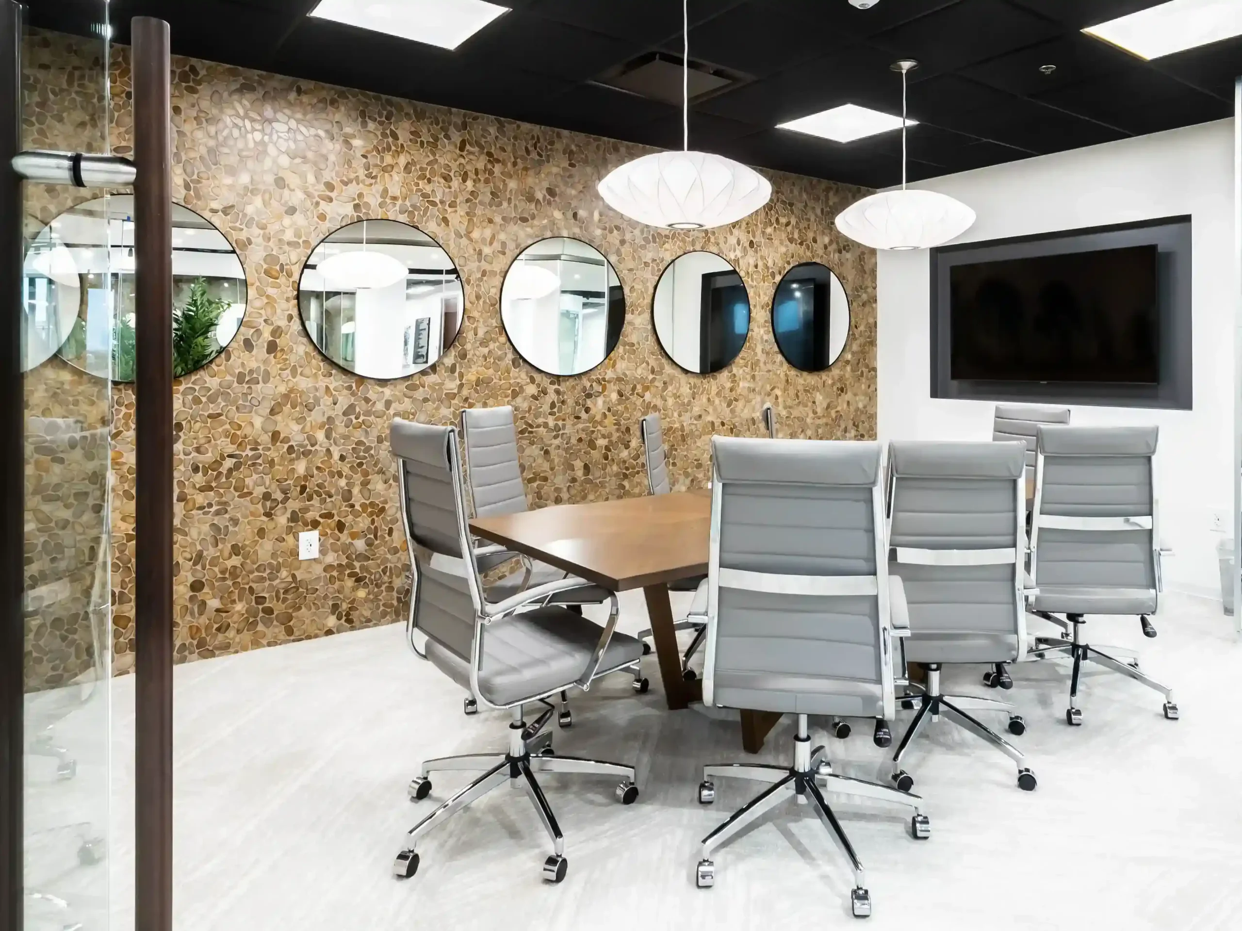 Meeting room with a wood table and gray chairs, a textured cork accent wall lined with round mirrors, and dome pendant lights