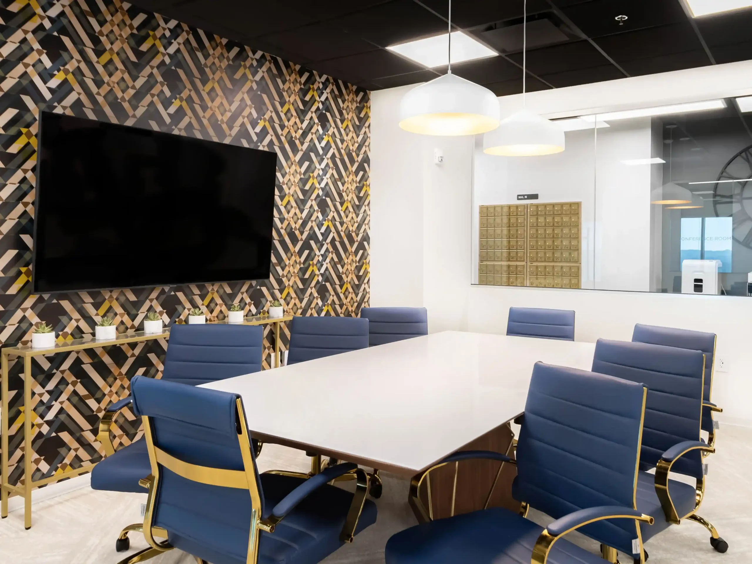 Conference room with a large wall-mounted TV, a patterned gold and navy accent wall, and navy blue chairs